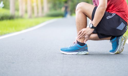 Young adult male with his muscle pain during running. runner man having leg ache due to Ankle Sprains or Achilles Tendonitis. Sports injuries and medical concept